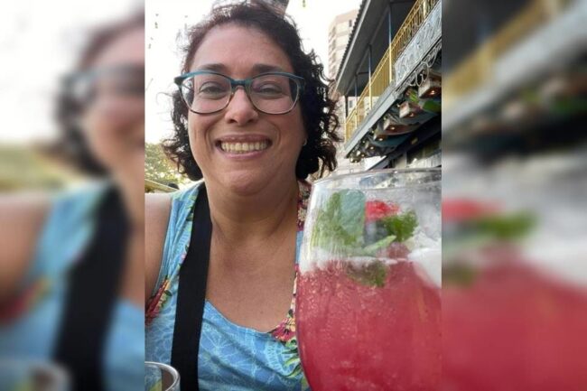 oscabecasdanoticia-psico-2 mulher com óculos cabelo curto com cachos roupa azul segurando um drink cor de rosa