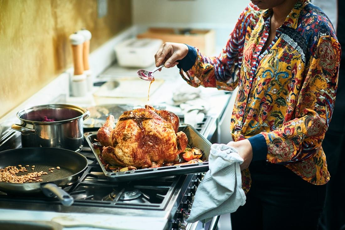 Mulher regando com molho um peru de natal na tábua para assar. O alimento está posicionado em cima de um fogão