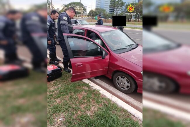 oscabecasdanoticia-crian Imagem mostra policiais em frente a carro vermelho, que está com a porta aberta - Metrópoles