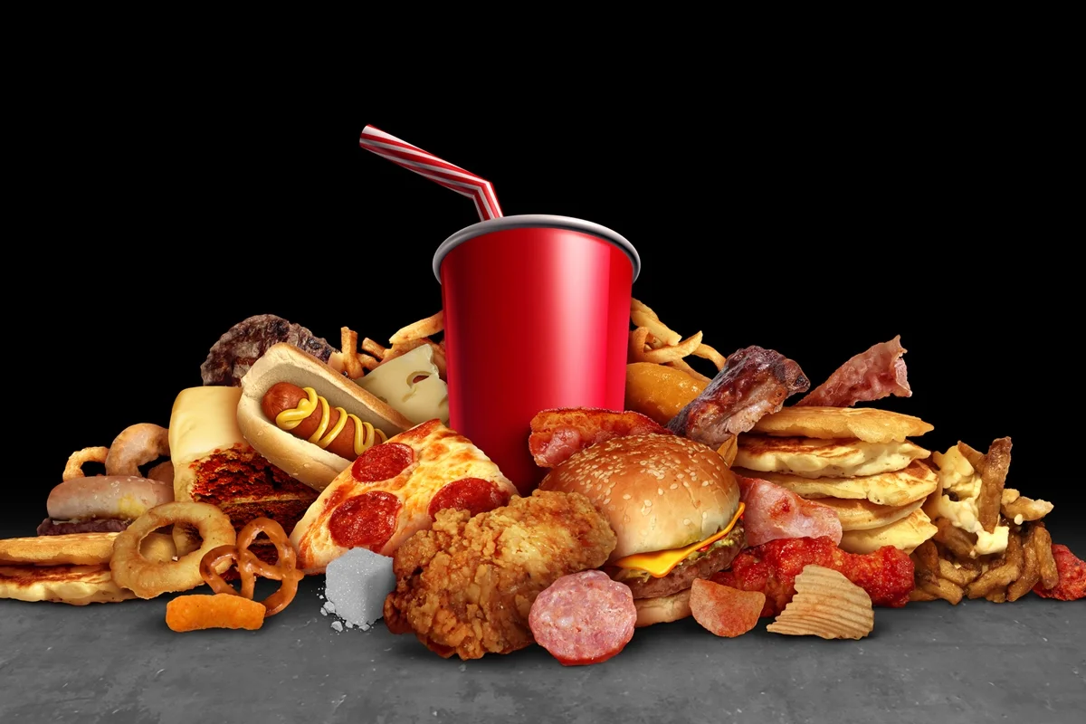 Alimentos processados ​​e calóricos, como frituras, hambúrgueres e refrigerantes, que acarretam riscos à saúde como obesidade e diabetes, devido ao alto teor de gorduras prejudiciais à saúde, em um fundo preto com elementos de ilustração 3D. Metrópoles